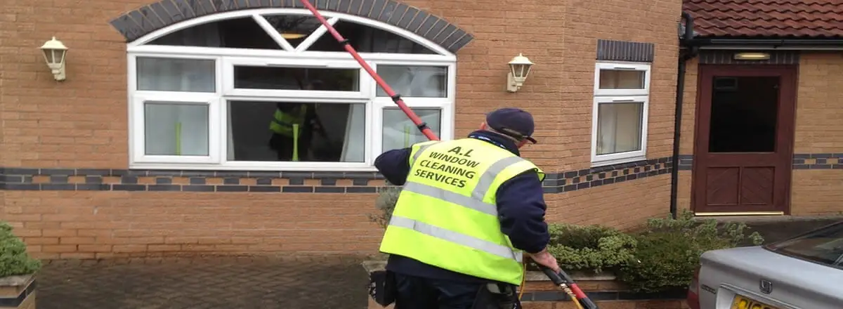 uniformed AL window cleaner using reach and wash pole on a house in Bolton